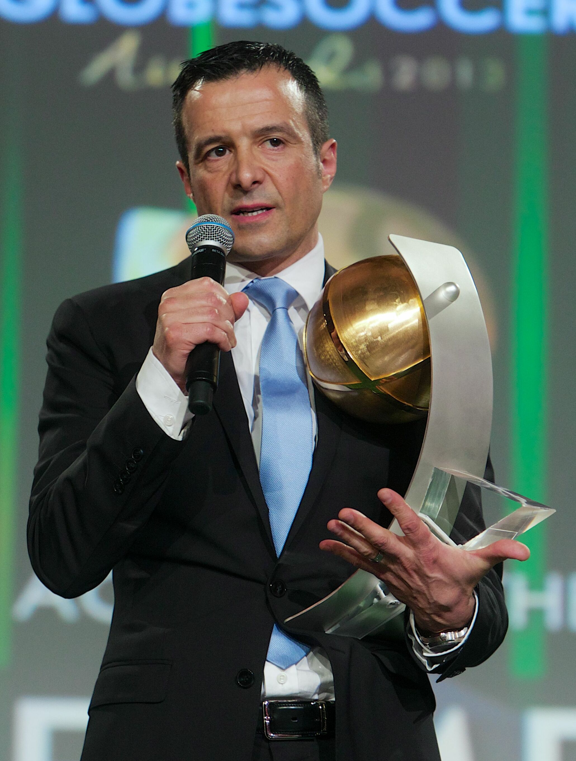 Jorge Mendes football agent speaking on stage while holding a large trophy during an awards ceremony.