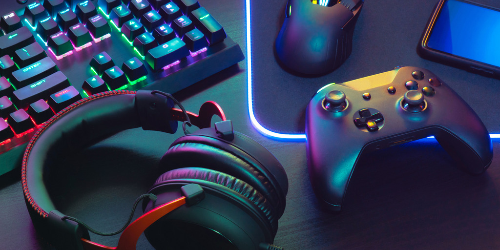 A modern gaming setup featuring a controller and headphones placed on a desk beside a glowing monitor.
