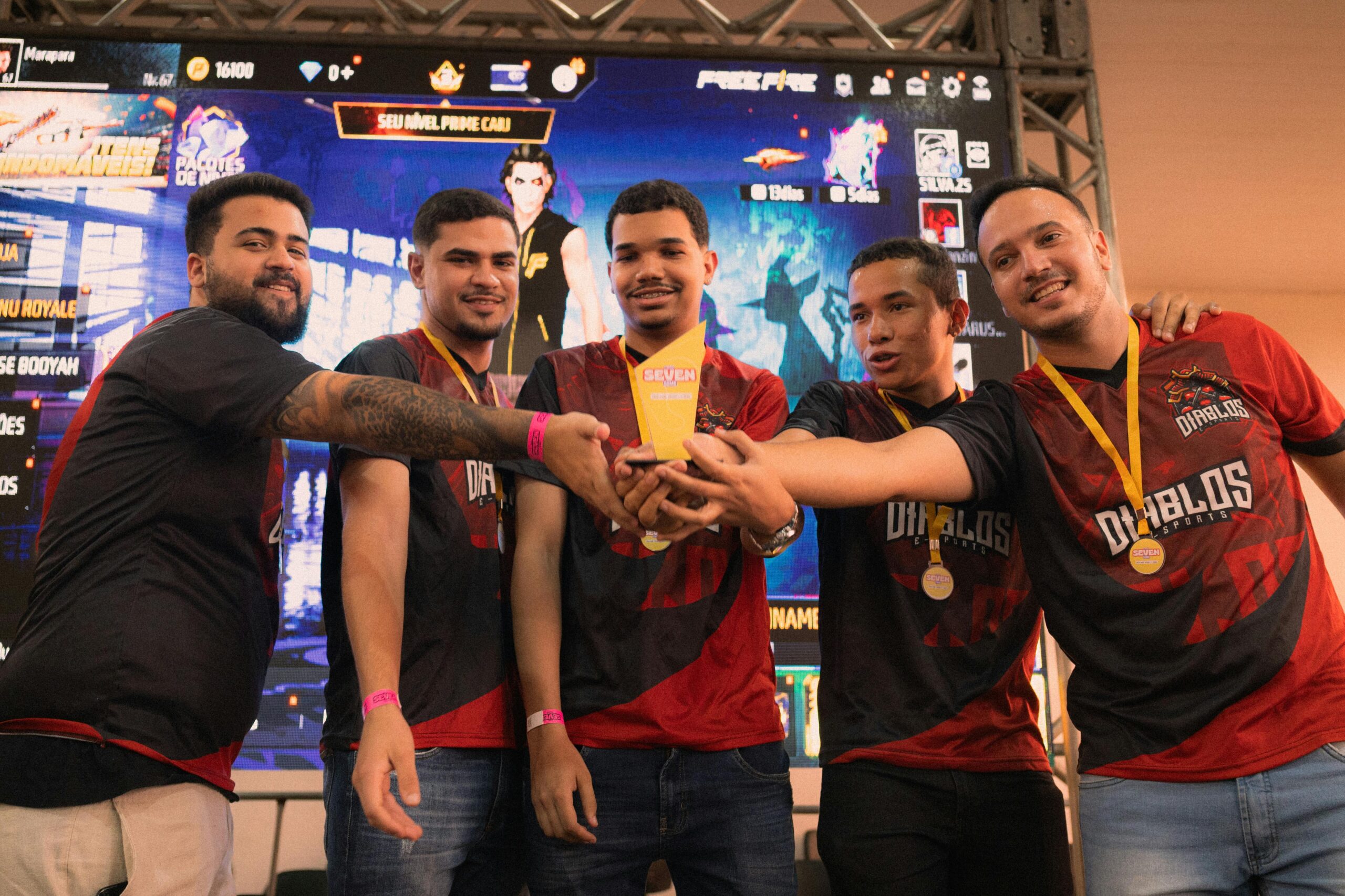 Esports team celebrating a tournament victory while holding a trophy together on stage.