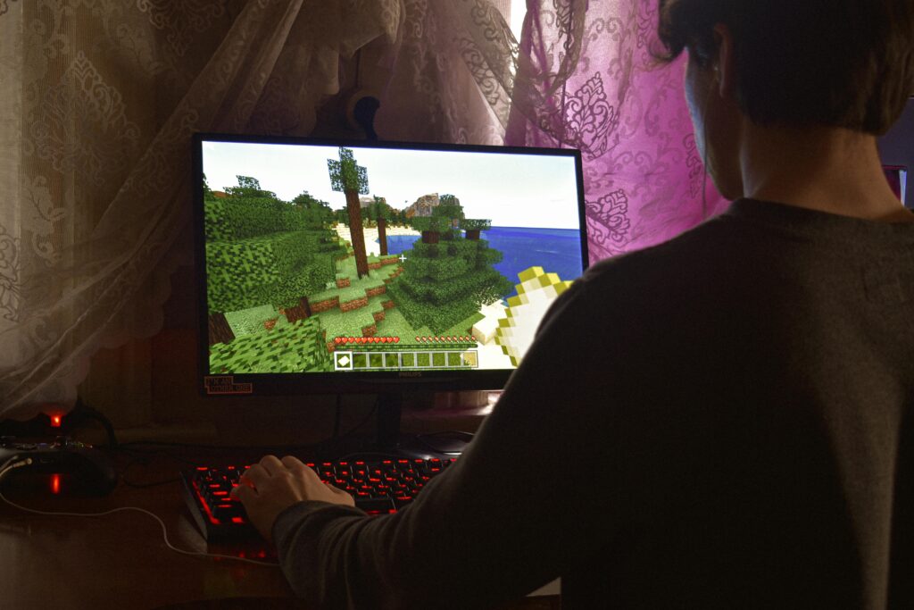 Player sitting at a desk using keyboard and mouse while playing Minecraft on a PC monitor.