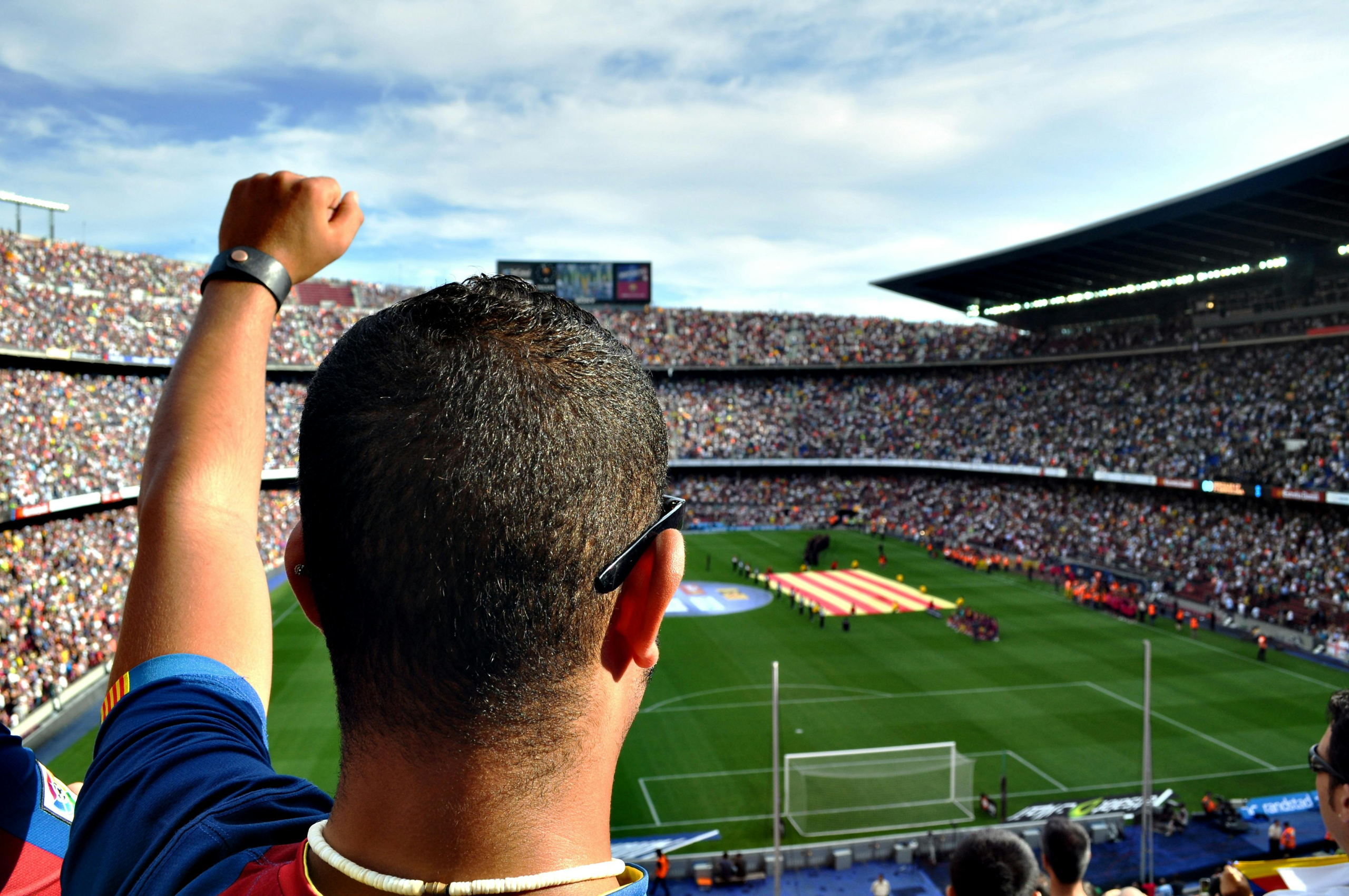 A fan raising their arm inside Camp Nou during a packed FC Barcelona match, overlooking the stadium and pitch.