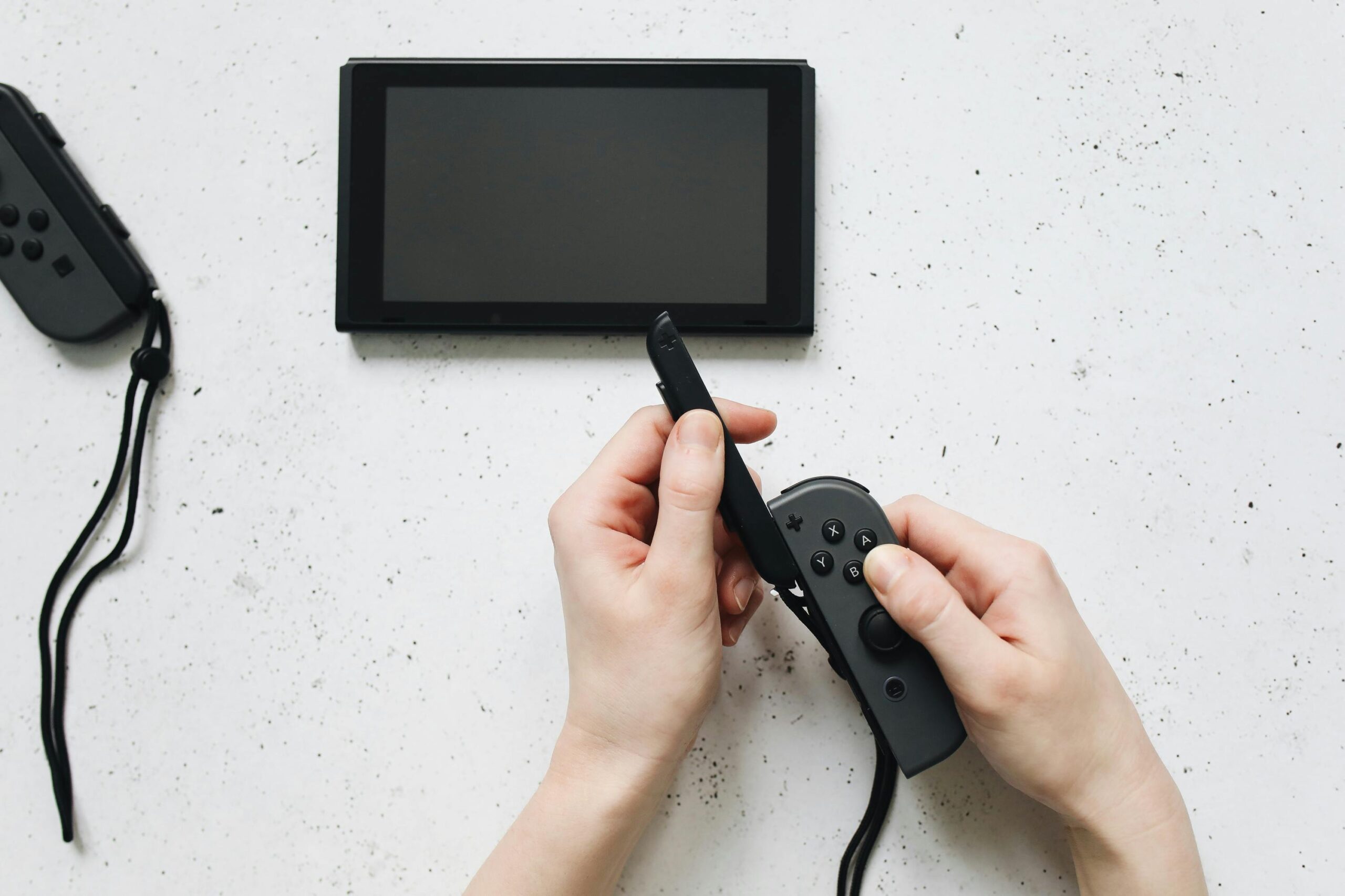 Hands attaching a Joy-Con controller to a Nintendo Switch console on a white table