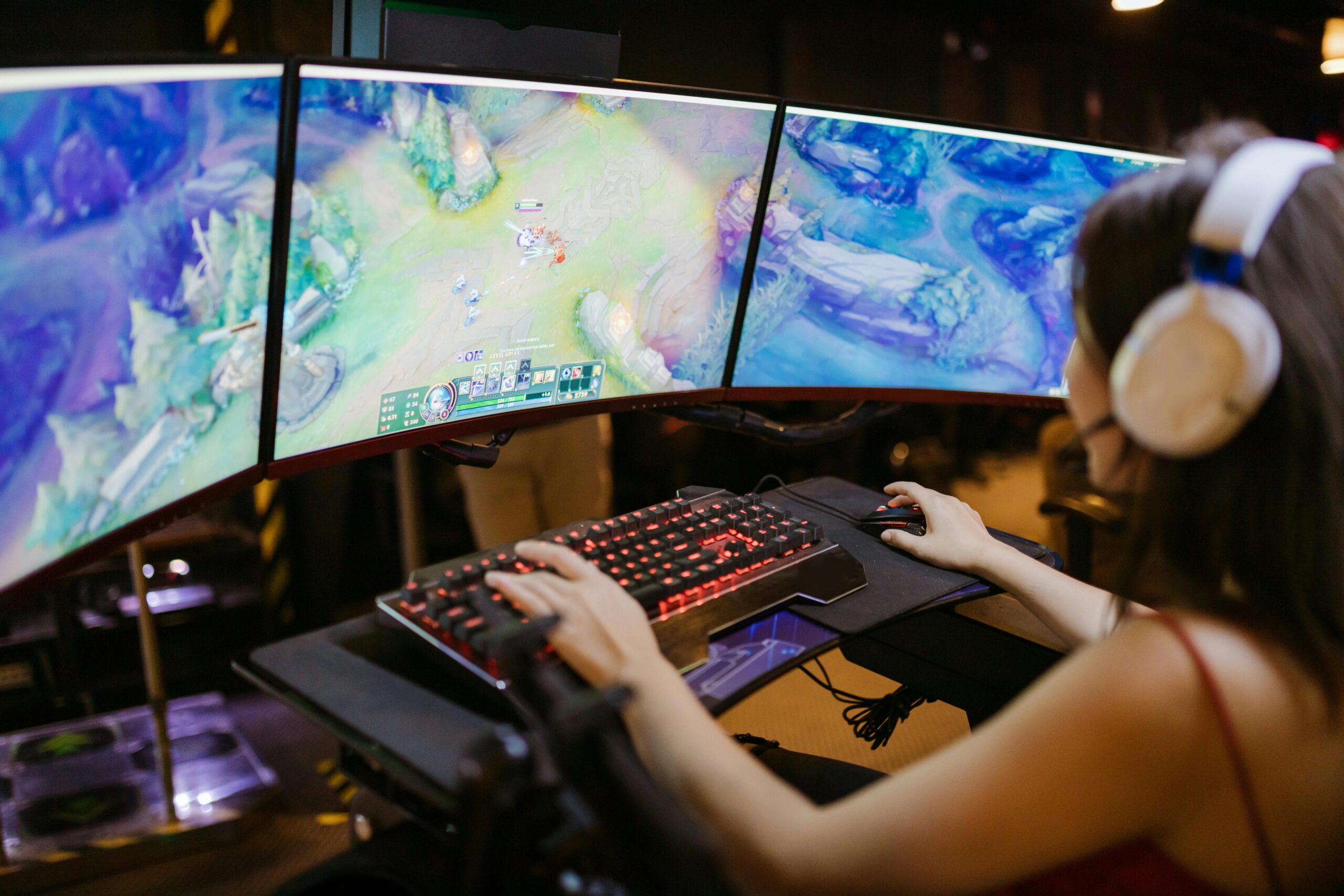 Esports player using a triple-monitor setup while playing a MOBA game during a competitive match.