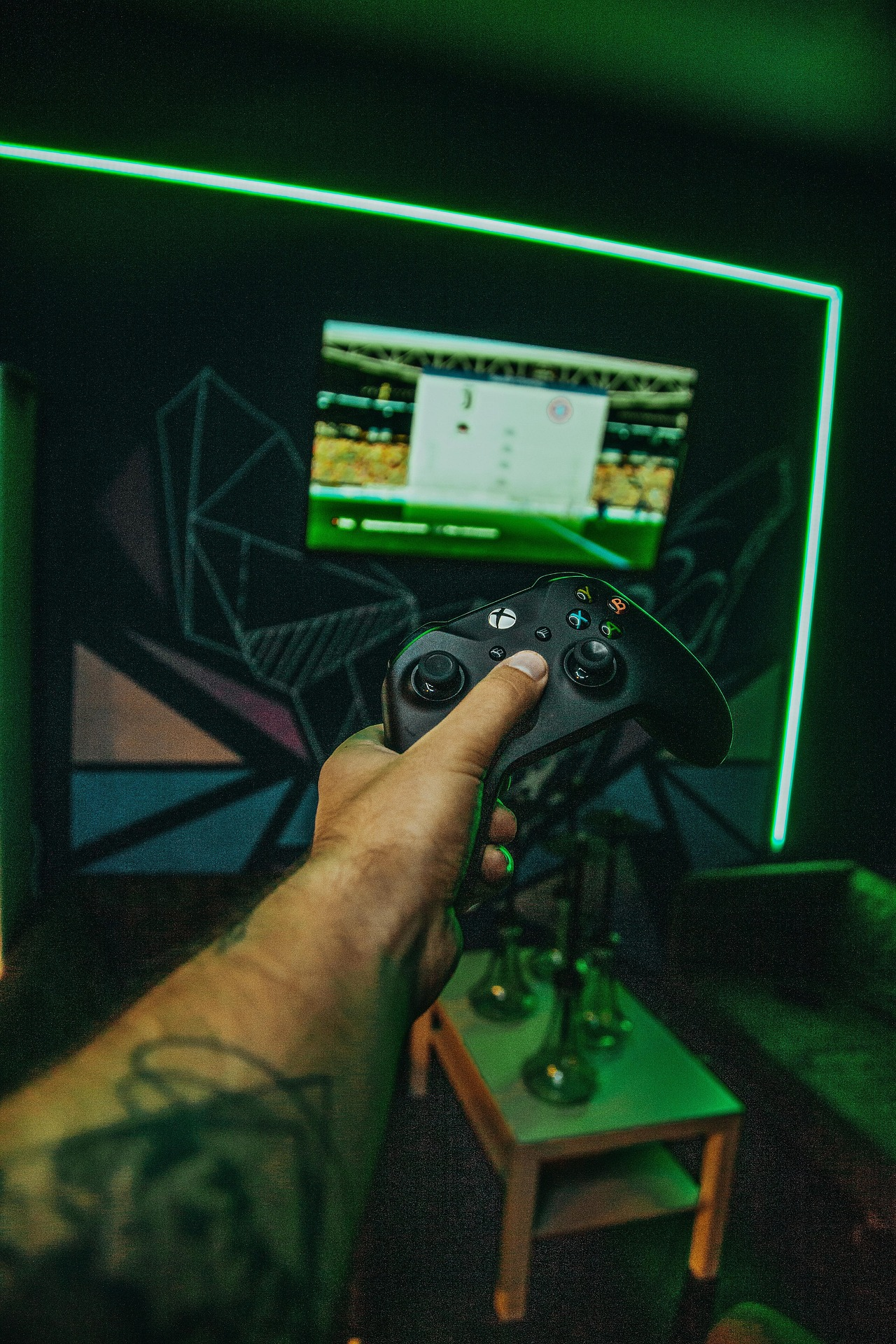 hand holding an Xbox controller in a neon lit gaming setup