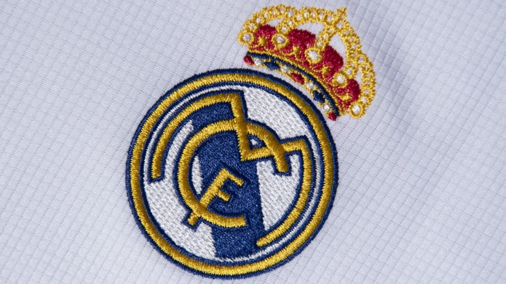 Real Madrid club badge featuring the royal crown and intertwined “MCF” initials on a white and gold crest.