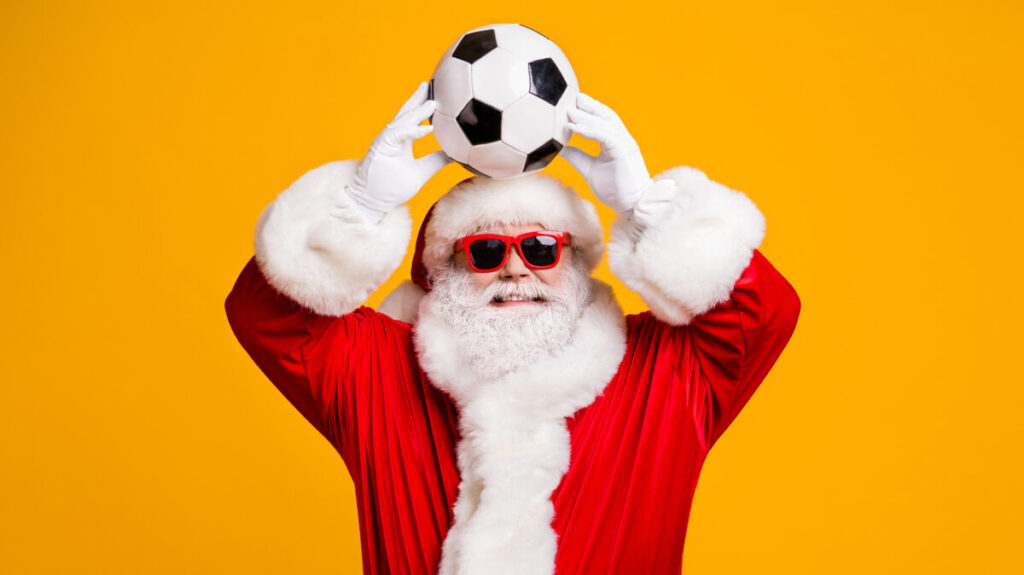 Santa Claus holding a football above his head against a yellow background