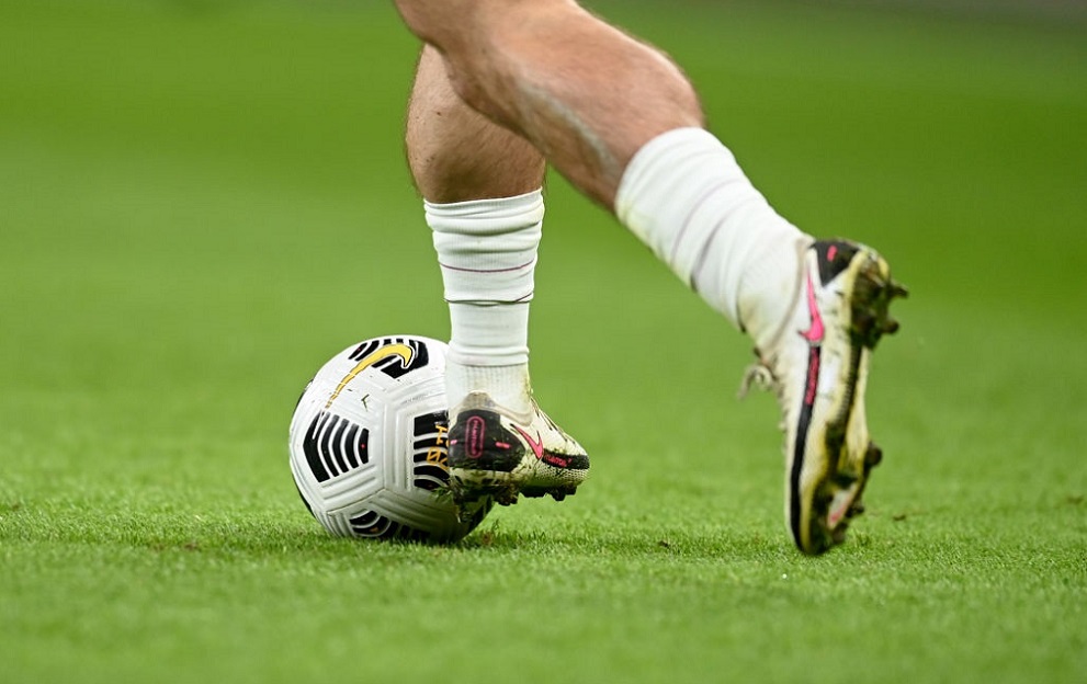 Close-up of a footballer controlling a ball during a match, showing boots and lower legs on the pitch.