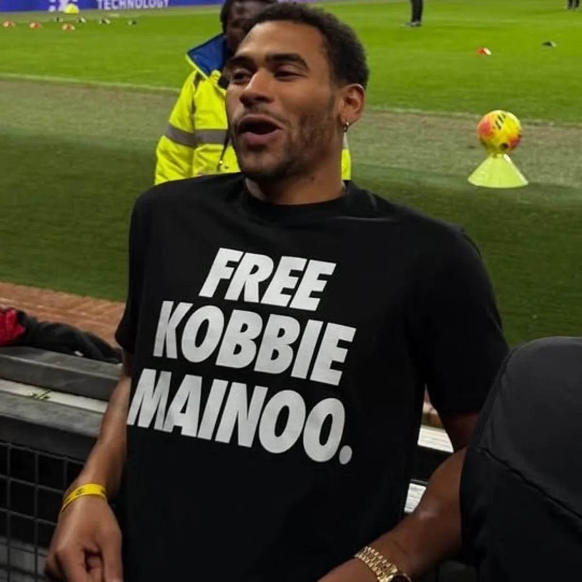 Jordan Mainoo-Hames wearing a 'Free Kobbie Mainoo' T-shirt in the stands during a Manchester United match.
