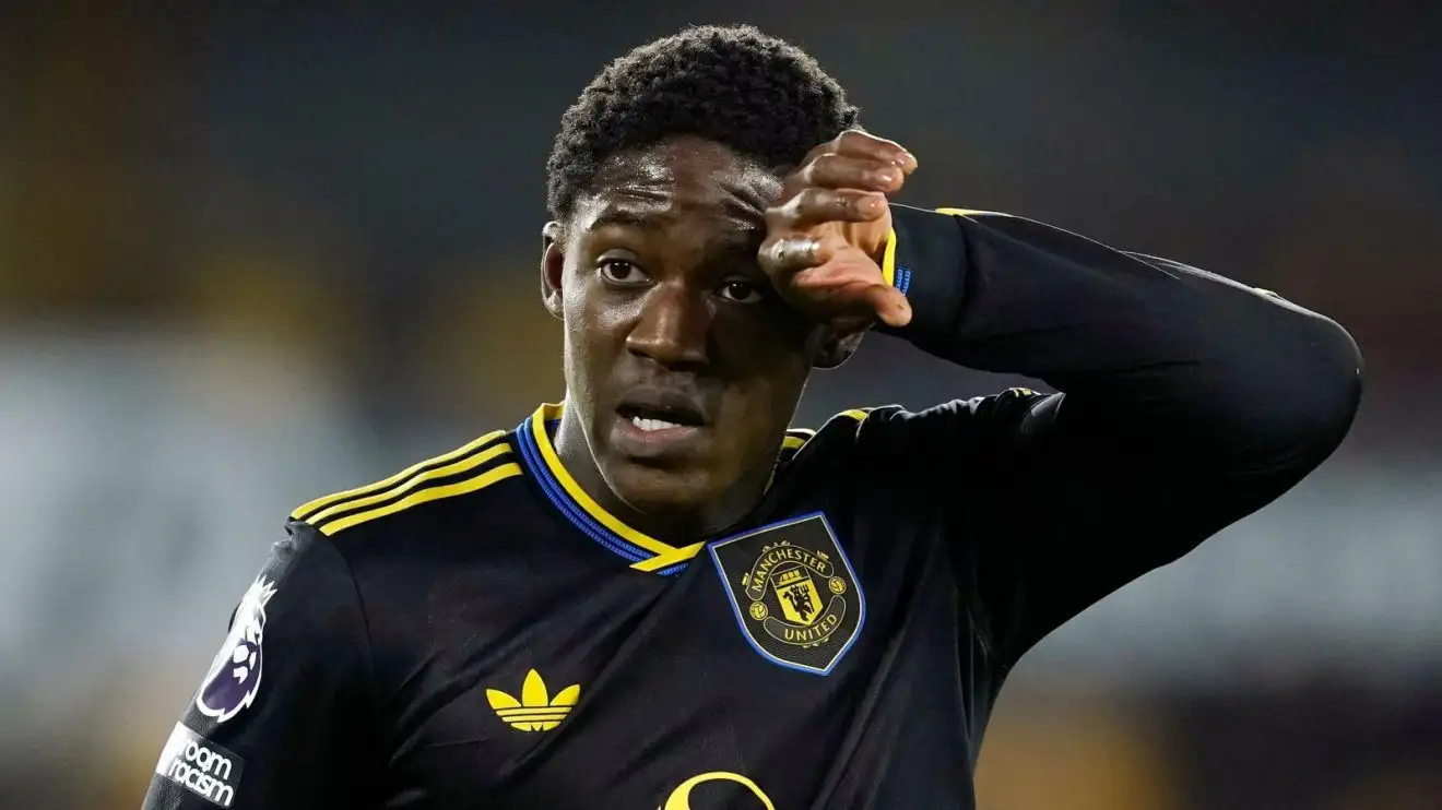 Kobbie Mainoo looking exasperated on the pitch during a Manchester United match, hands on hips as play continues.