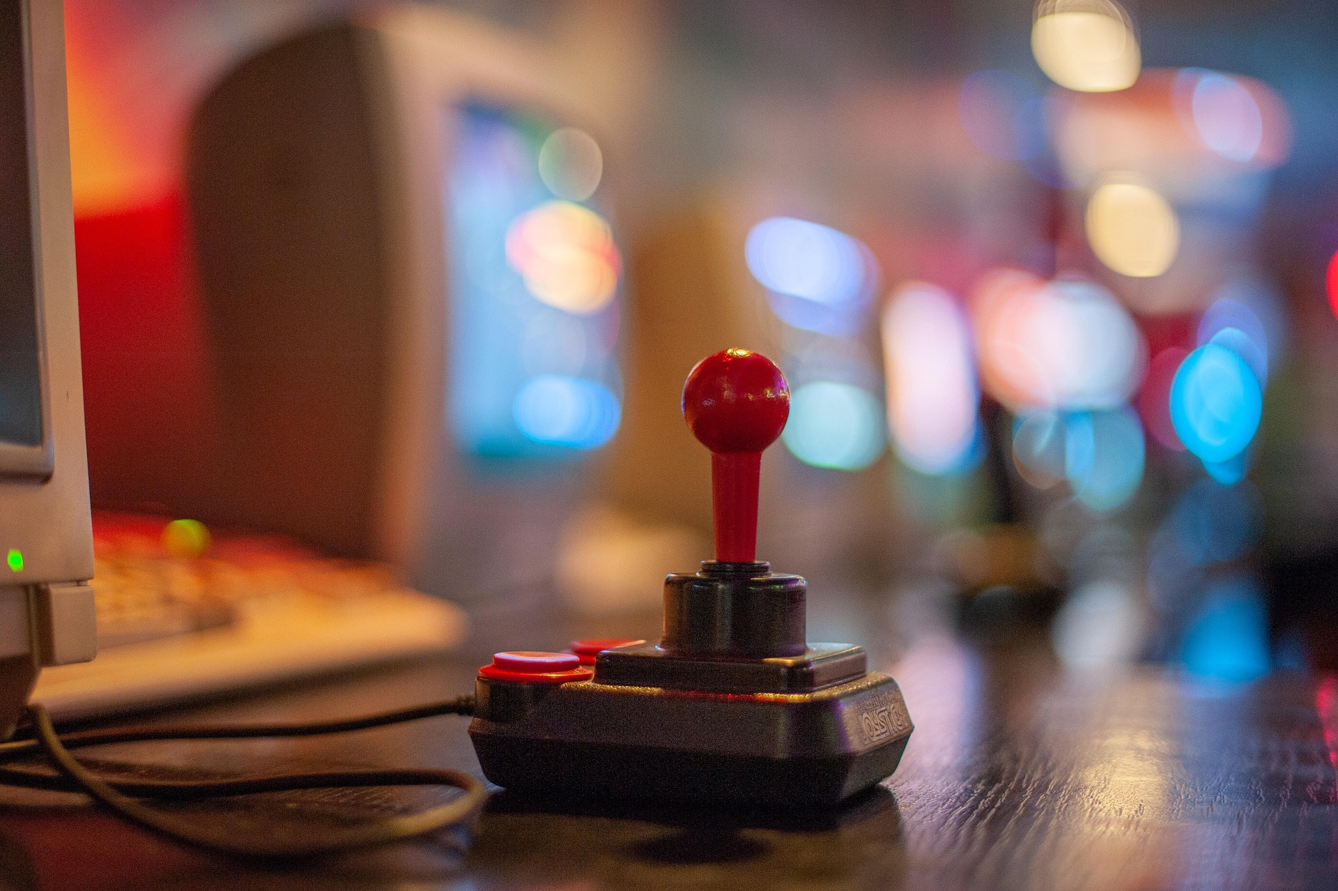 Classic arcade joystick on a table with retro gaming machines in the background