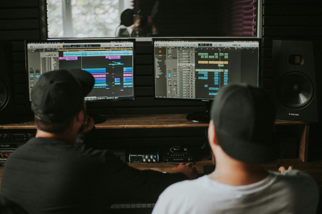 Two audio engineers working on sound design and music production using dual computer monitors in a studio.