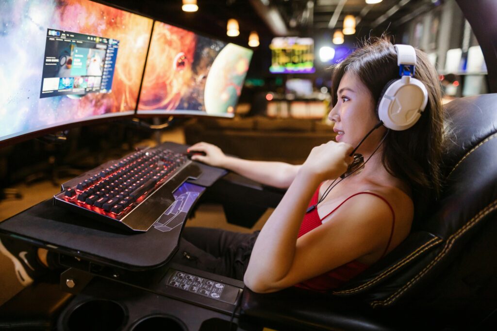 Female streamer gaming at a dual curved monitor setup with a mechanical keyboard and headset.