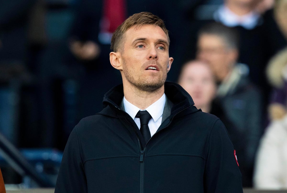 Darren Fletcher wearing formal attire in the stands at a Manchester United match, observing the game attentively.