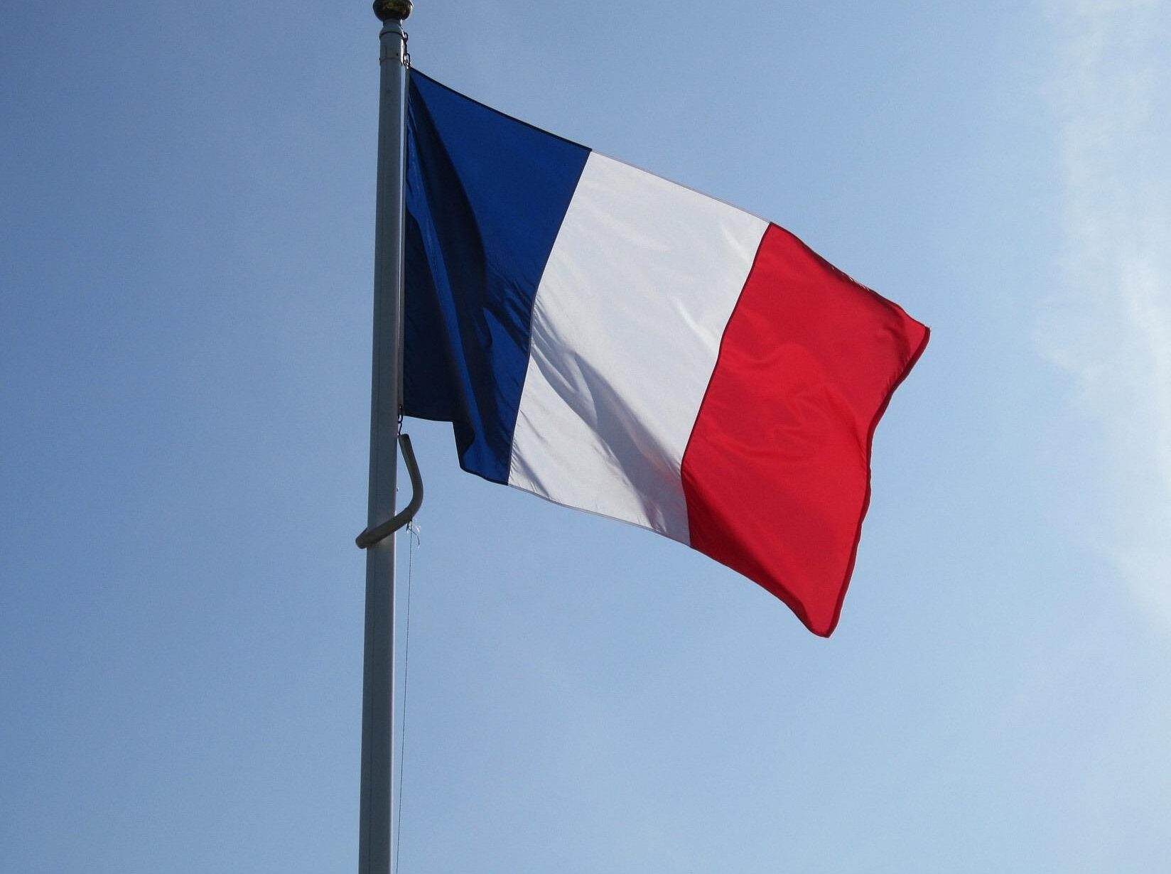 French national flag flying on a flagpole against a clear blue sky