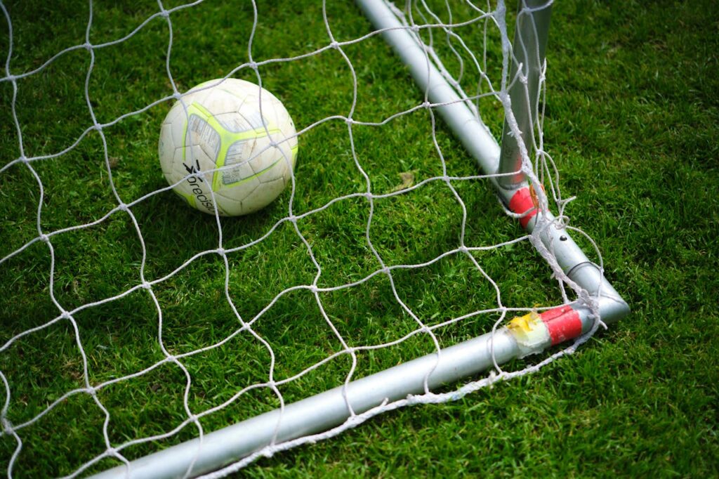 Close-up image of a football resting in a goal net on a vibrant green grass field.