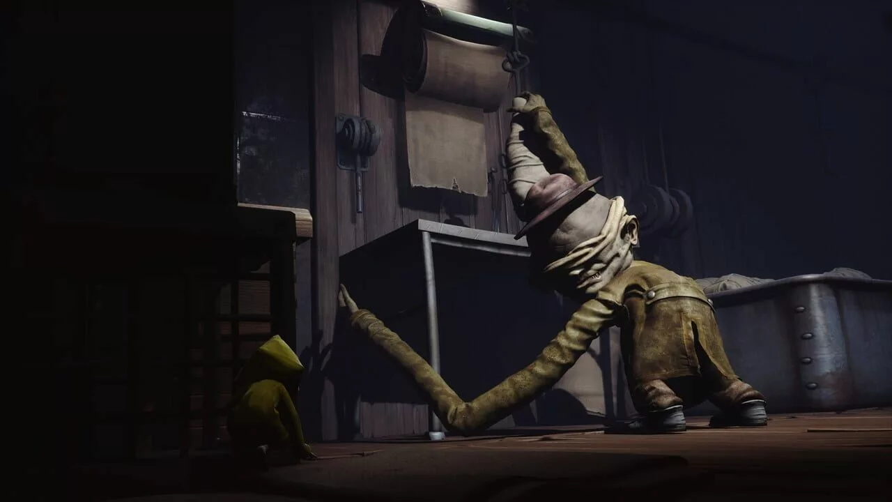 A gameplay screenshot from Little Nightmares showing the protagonist Six hiding from the Janitor, a long-armed monster wearing a hat and blindfold.
